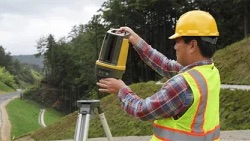 Surveyor operating a handheld scanner beside a road